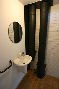 煙突はストーブの裏の耐火煉瓦の壁を抜けトイレの中で立ち上がってます。左側が煙突、右側は床下換気用のダクトです。左側壁のの黒く塗られた部分がビス留めで外せるようになっており壁内を確認出来ます。