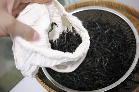 蒸して熱々の茶葉を手で袋に詰める